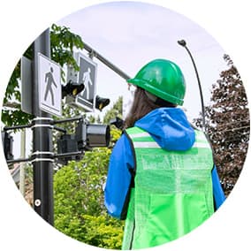 An ICBC engineer wearing a reflective vest and hardhat who is standing at a pedestrian crossing.